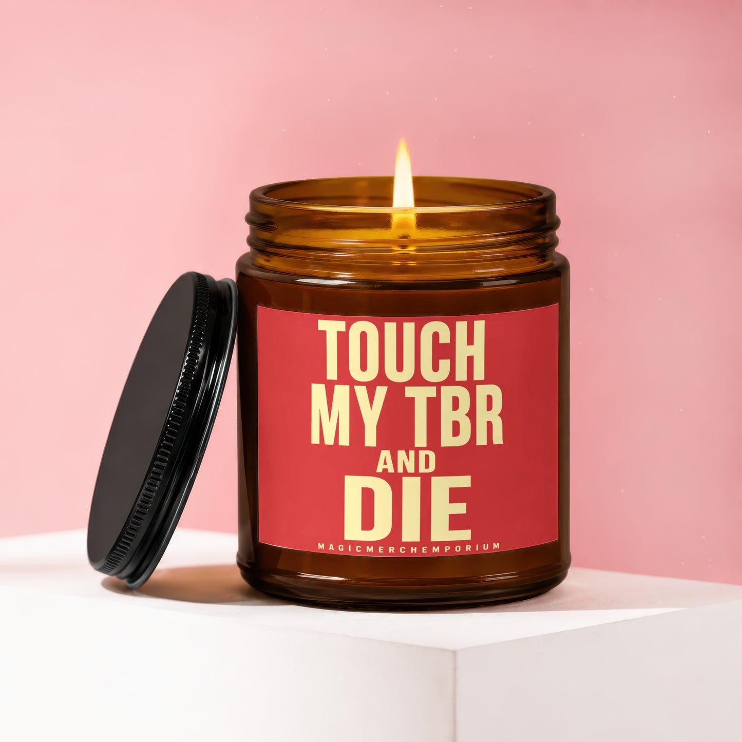 A lit amber glass candle with a red label reading "TOUCH MY TBR AND DIE"