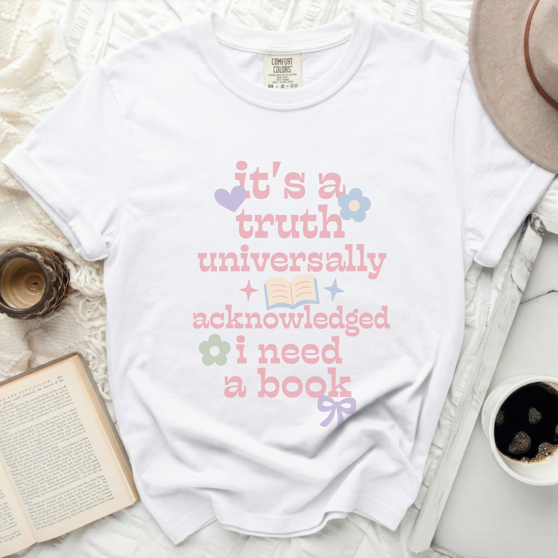 White t-shirt with pastel graphic text: it's a truth universally acknowledged i need a book.