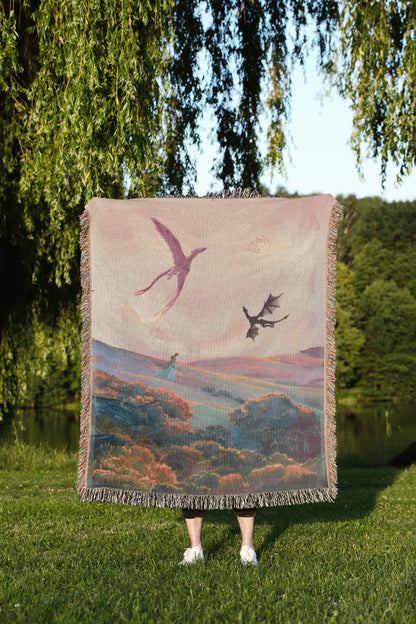 A person stands in a grassy field, holding a large woven blanket with a painting of a bird and a dragon on it.