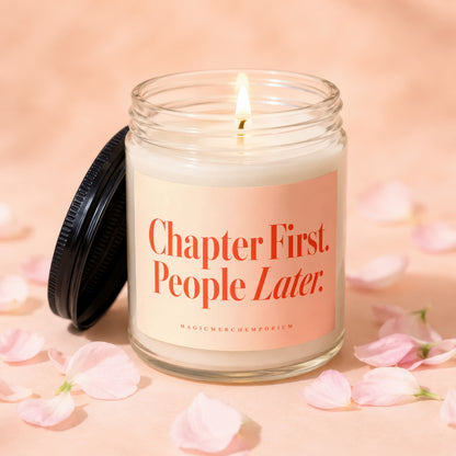 Glass jar candle with lit wick and a pink label reading "Chapter First. People Later."