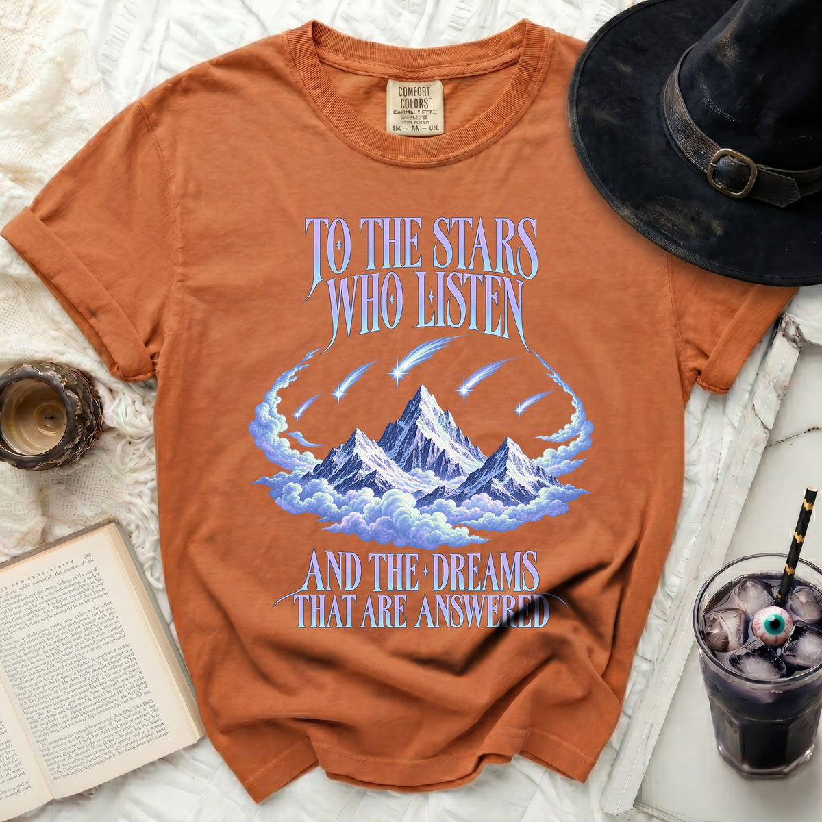 Orange t-shirt with mountains, clouds, comets, and text "TO THE STARS WHO LISTEN AND THE DREAMS THAT ARE ANSWERED".