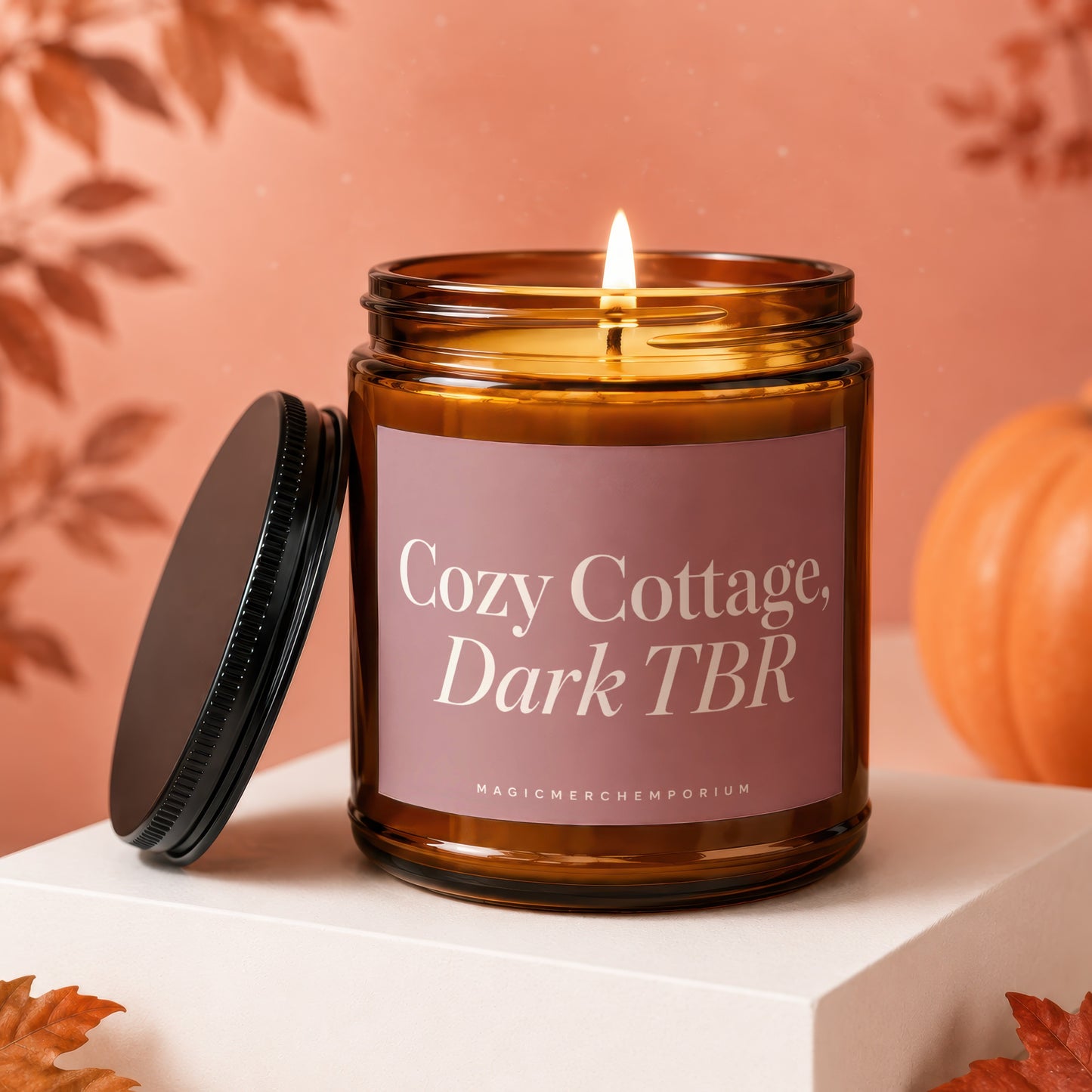 Lit amber candle with "Cozy Cottage, Dark TBR" label and black lid, on a white pedestal.