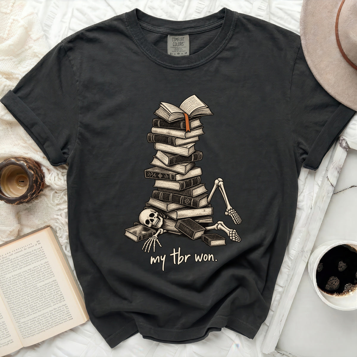 Dark grey t-shirt with skeleton buried under books and text "my tbr won."