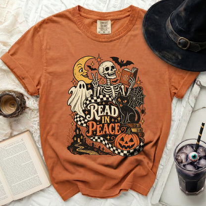 Orange t-shirt with Halloween graphic featuring skeleton, ghost, cat, moon, and text "Read In Peace".