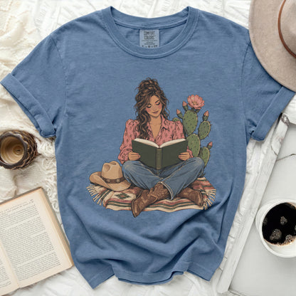 Graphic of woman reading with cowboy hat, boots, cactus, and patterned blanket.