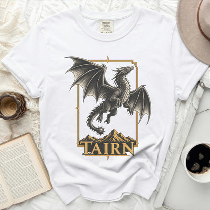 White t-shirt with a gold-framed graphic of a dragon over mountains and the word "TAIRN".
