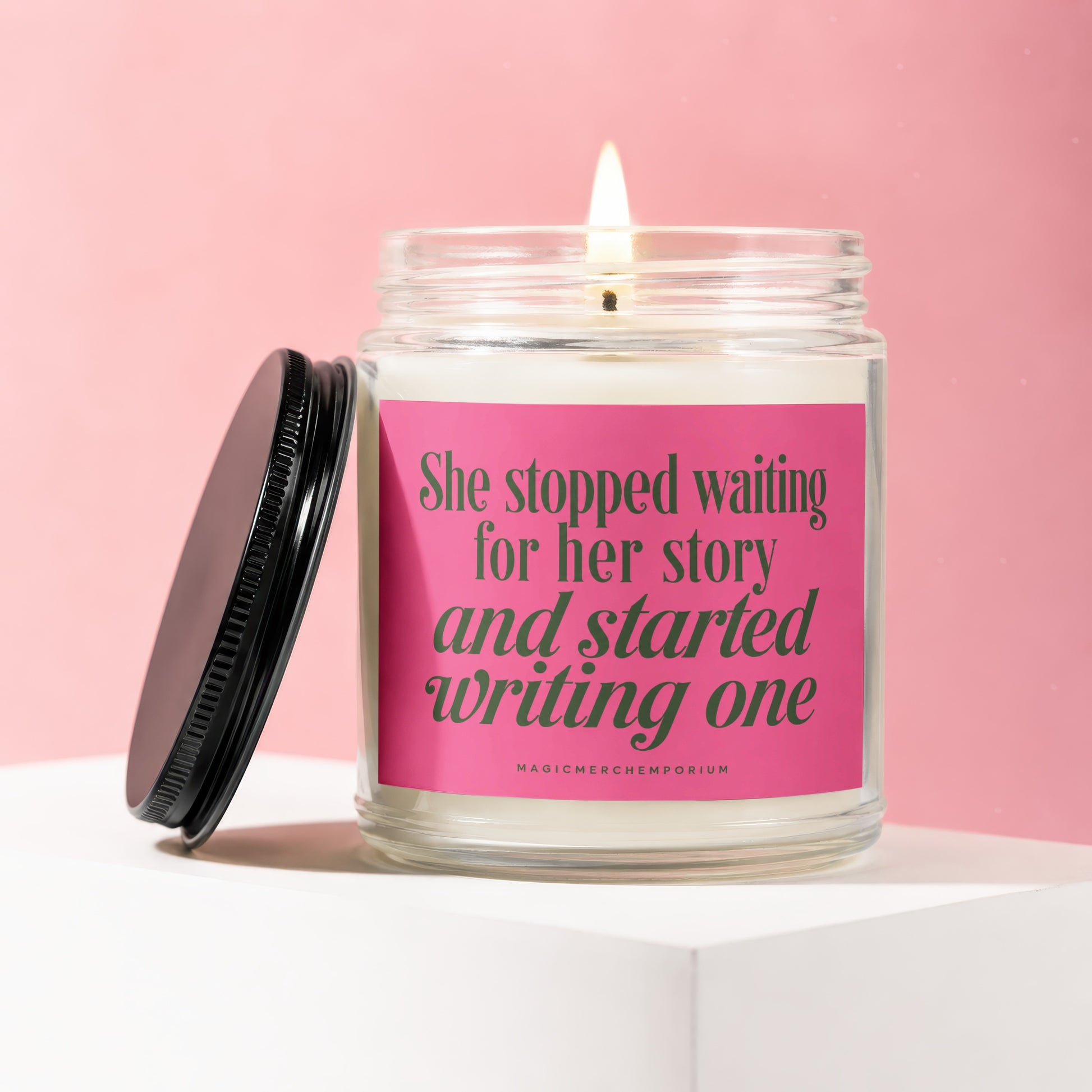 Lit candle in glass jar with pink label reading "She stopped waiting for her story and started writing one".
