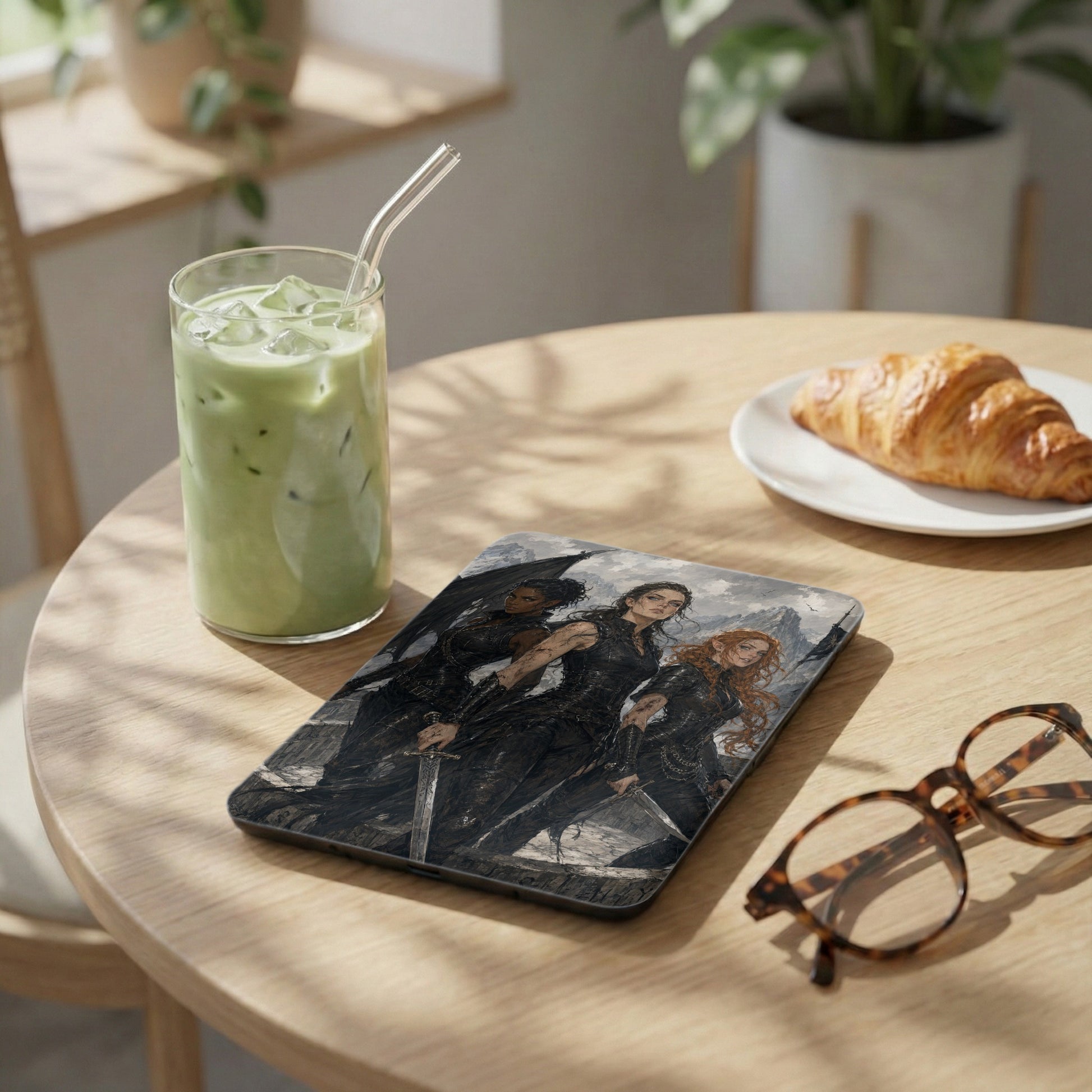 Tablet cover with three fantasy women holding swords, next to a matcha drink and croissant.
