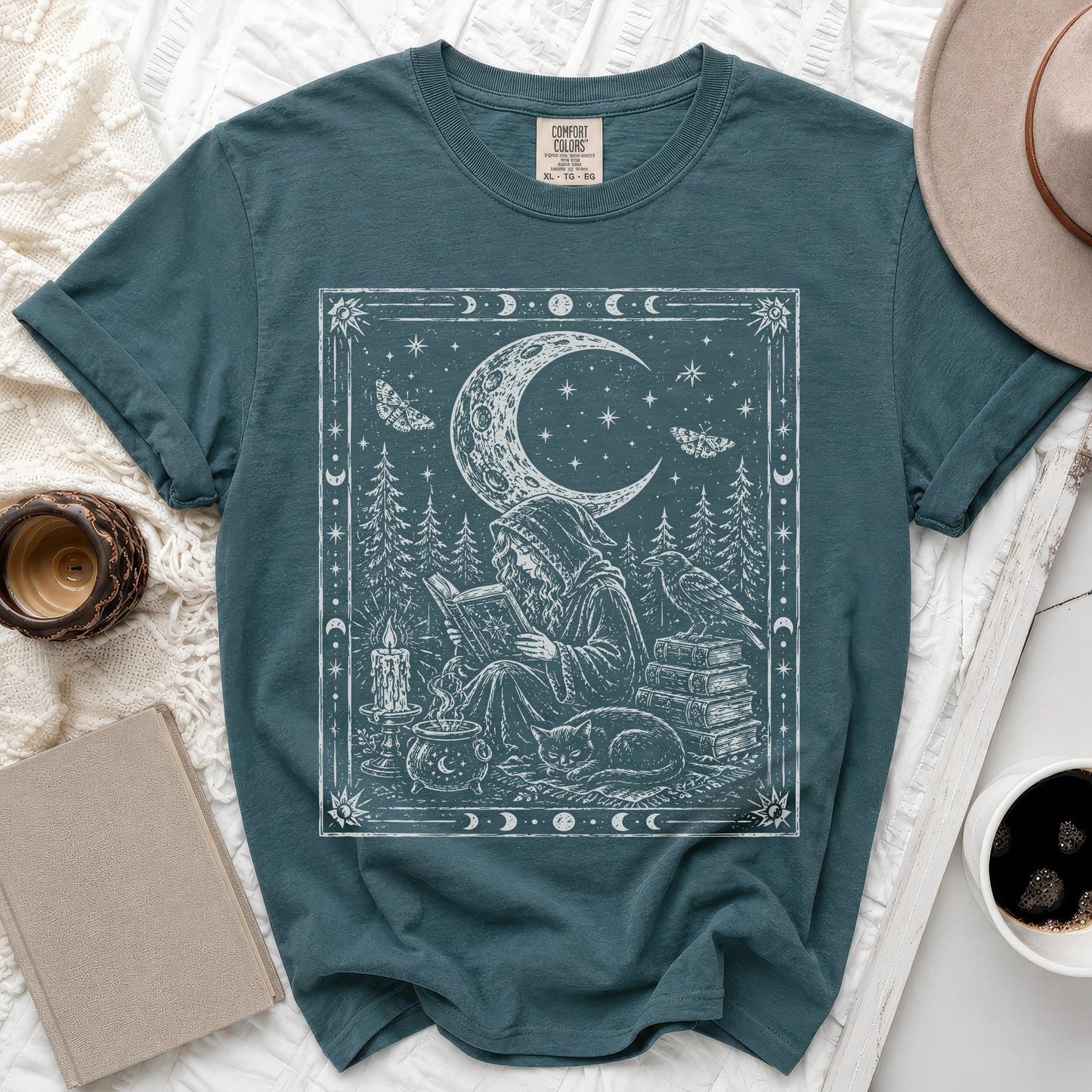 Dark teal t-shirt with white mystical graphic of a sorcerer reading by a cauldron.