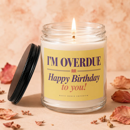 Lit candle in glass jar with "I'm Overdue Happy Birthday" label and black lid.