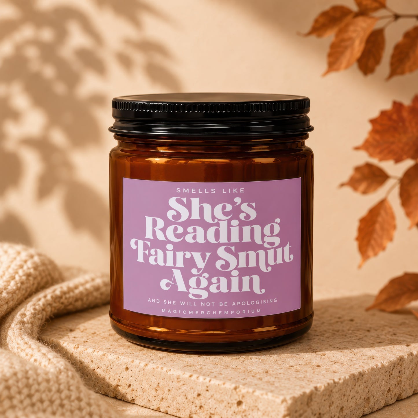 Amber jar candle with purple label reading "Smells Like She's Reading Fairy Smut Again."