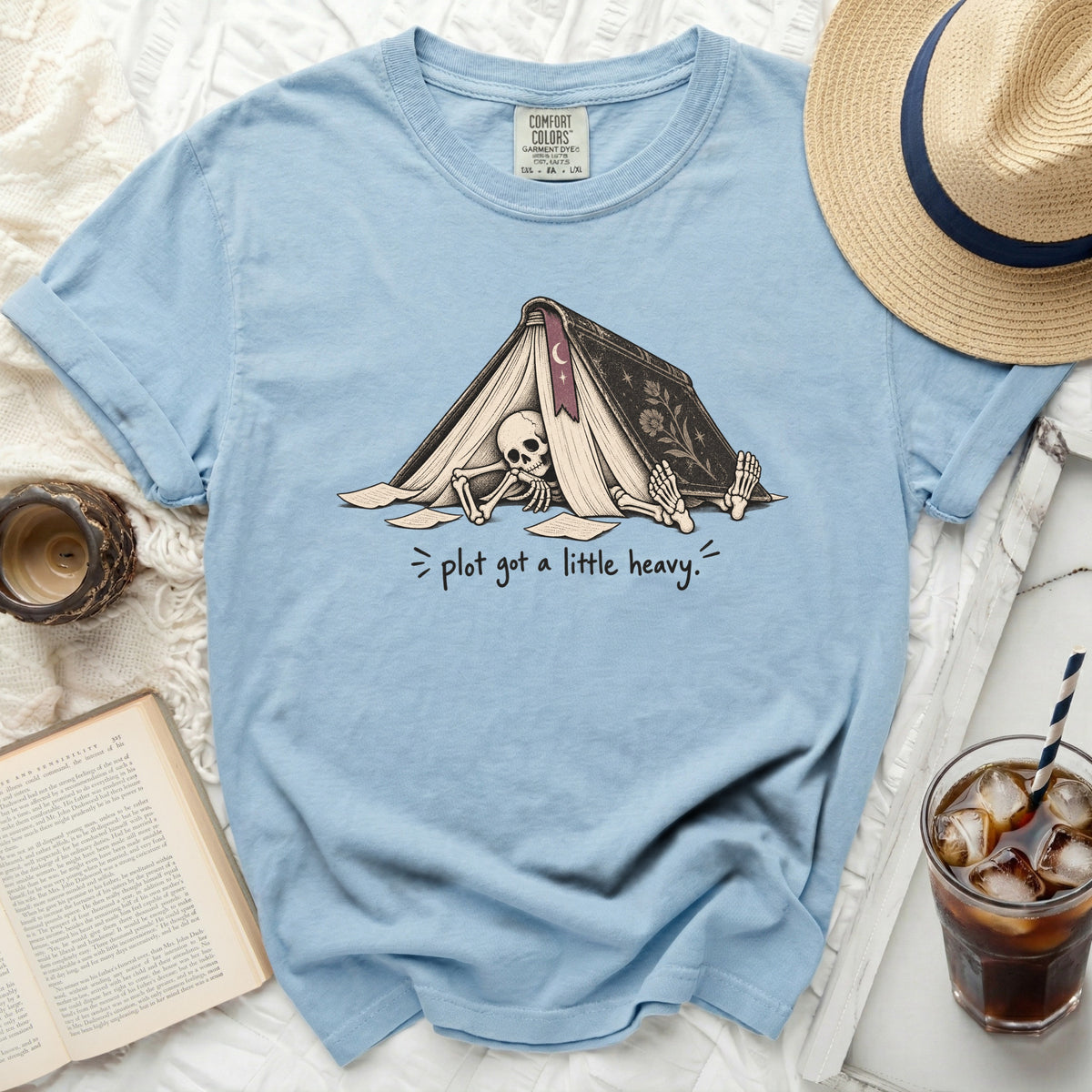 Light blue t-shirt with skeleton under a book and text "plot got a little heavy."