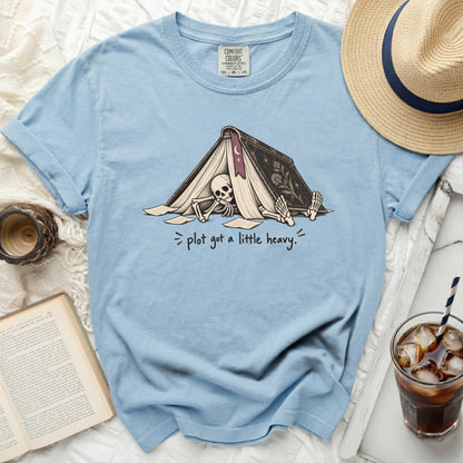 Light blue t-shirt with skeleton under a book and text "plot got a little heavy."