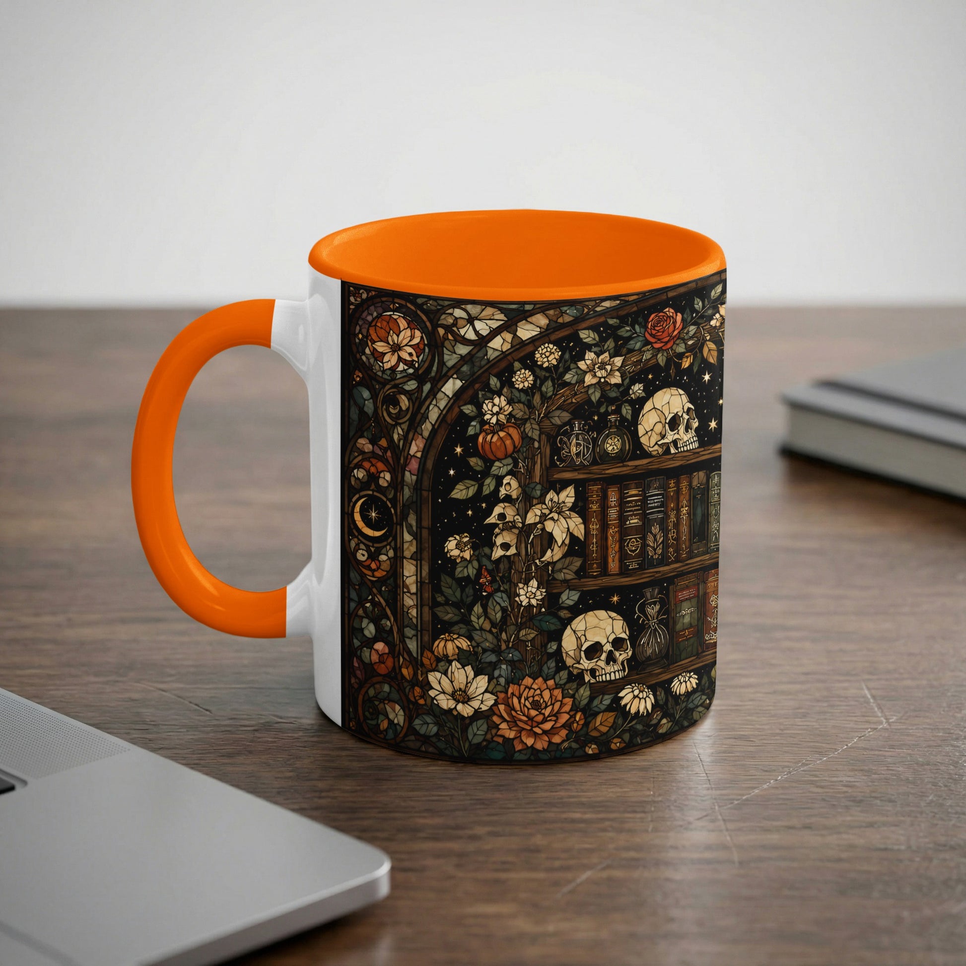 White mug with orange handle featuring a dark, stained-glass style design of books, skulls, and flowers.