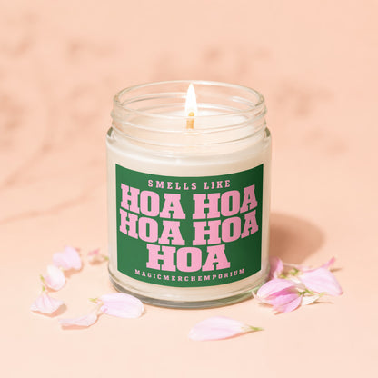 Scented candle with "Smells Like Hoa Hoa Hoa Hoa" text, lit flame, pink petals.