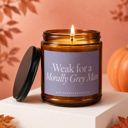 Amber glass candle with lit flame, purple label reads "Weak for a Morally Grey Man," lid off.