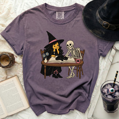 Witch, skeleton, and cat sit at a table with a book.