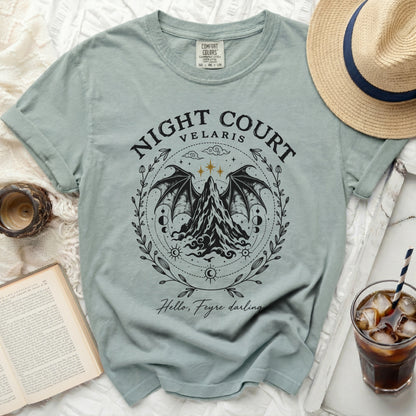 A sage green t-shirt with a black graphic of mountains, wings, and Night Court Velaris text.