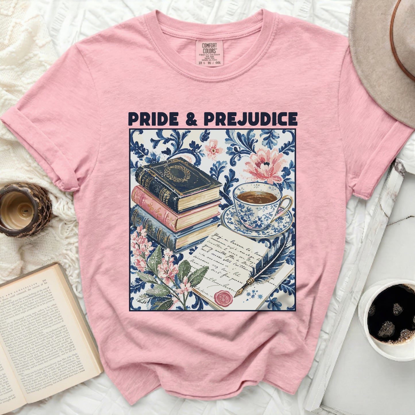 Pink t-shirt with "Pride & Prejudice" text and a vintage book stack, teacup, quill, and floral print.