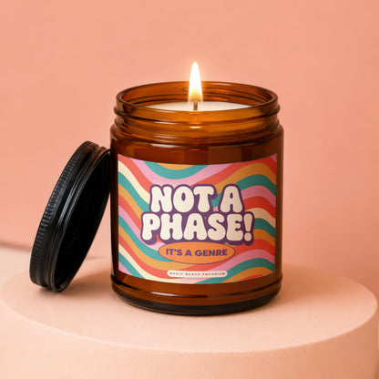 Amber jar candle with lit wick, "Not A Phase! It's A Genre" label.