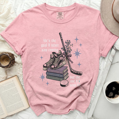 Pink t-shirt with books, hockey stick, and text "He's the goal I never saw coming but the one I'd stop for".