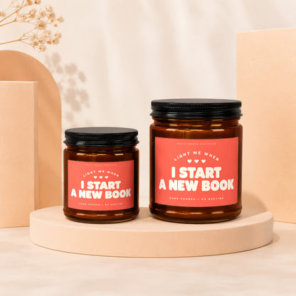 Two amber glass candles with red labels reading "Light Me When I Start A New Book".