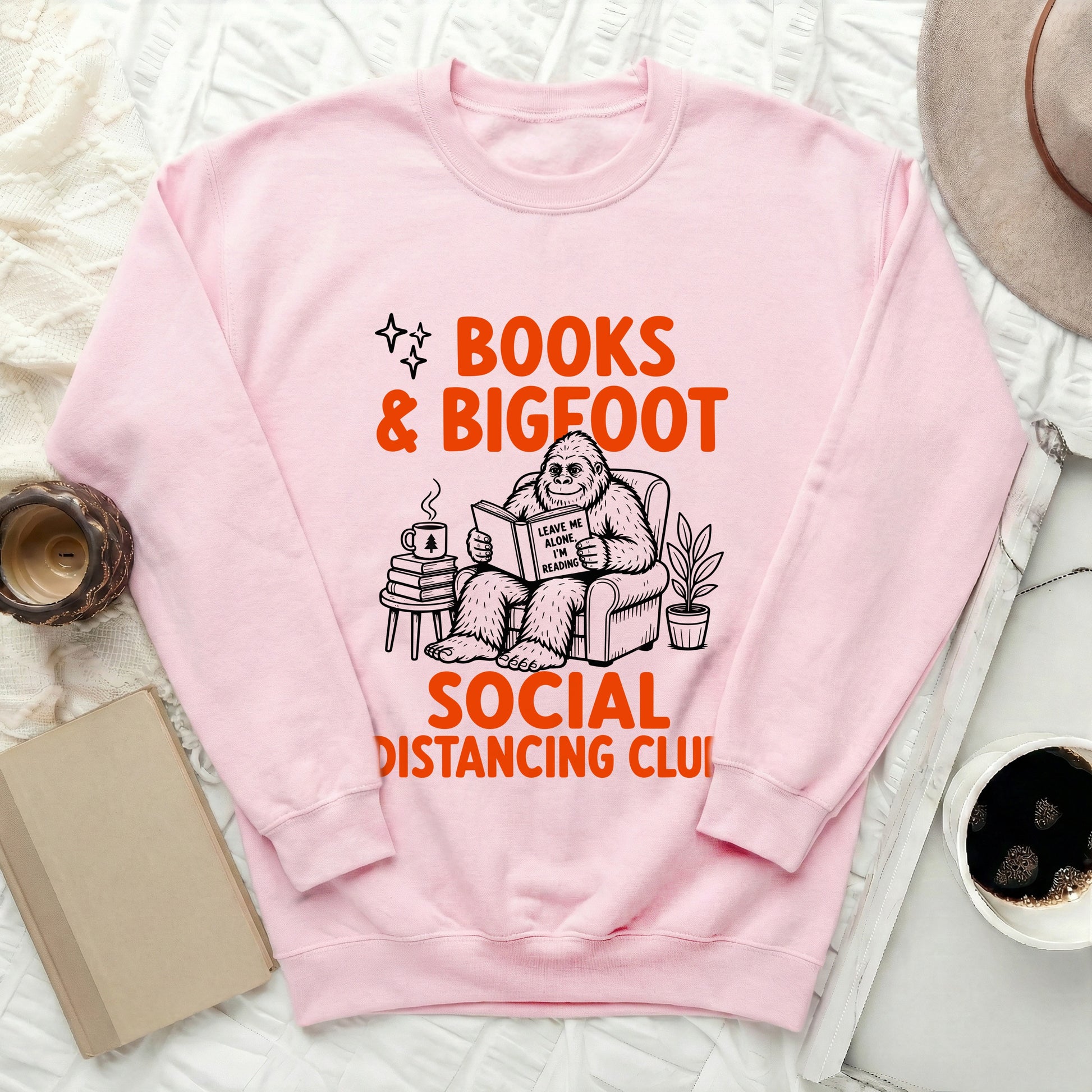 Pink sweatshirt with Bigfoot reading a book on a chair: "Books & Bigfoot Social Distancing Club".