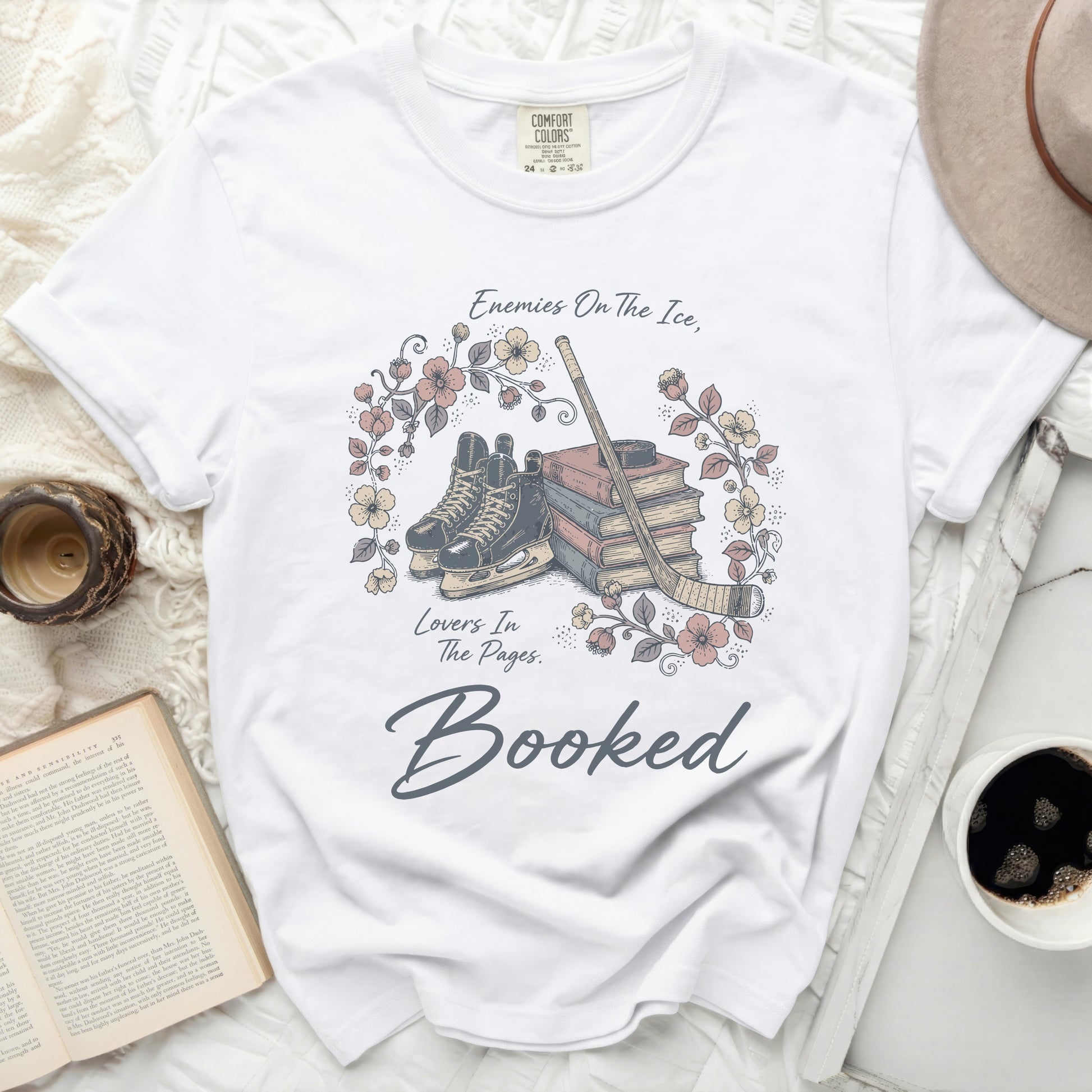 White t-shirt with stacked books, ice skates, and floral accents, "Booked" text.