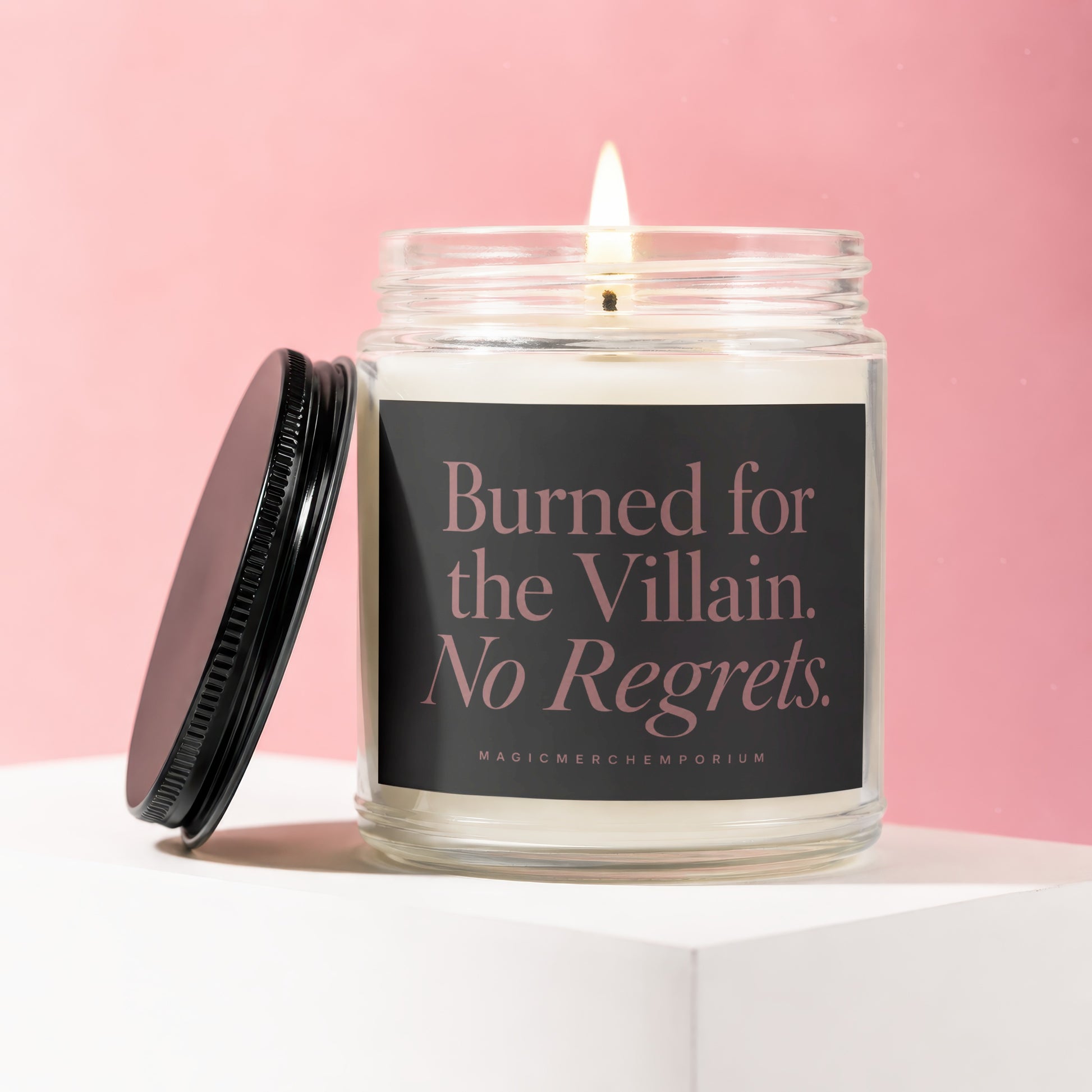 Candle with "Burned for the Villain. No Regrets." text burning on a pink background.