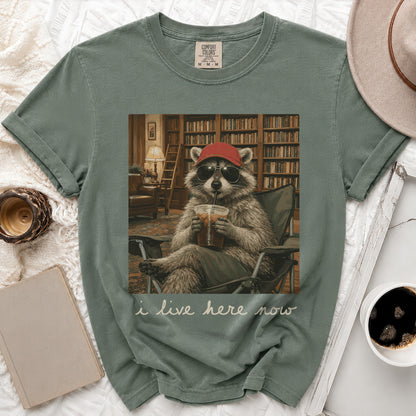 Green t-shirt with graphic of raccoon wearing sunglasses and hat drinking from cup.