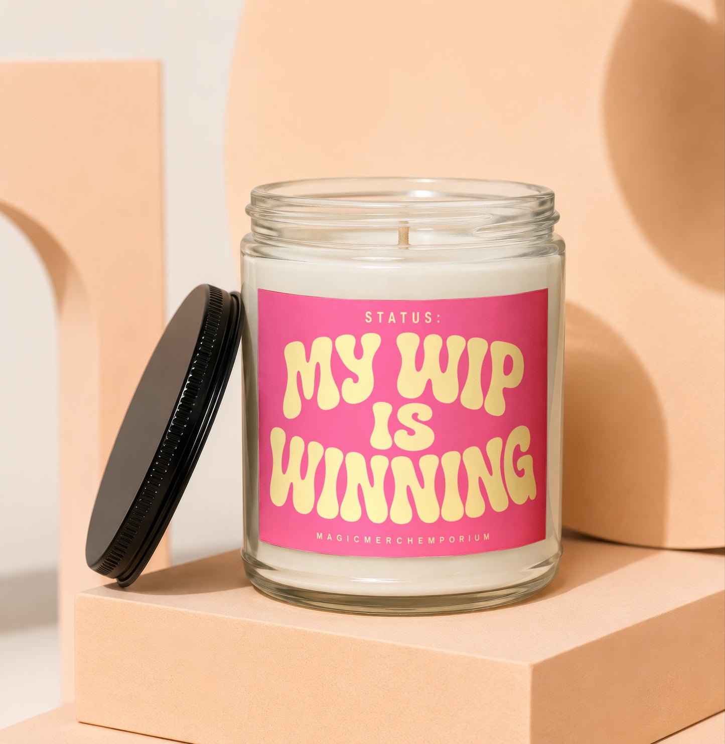 Glass candle with pink label reading "STATUS: MY WIP IS WINNING"