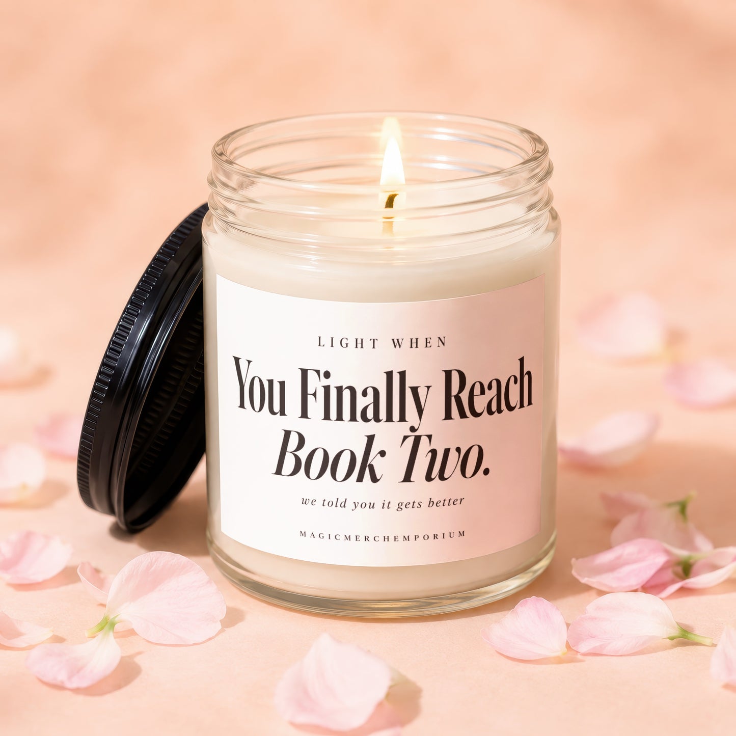 A lit candle in a glass jar with a black lid, surrounded by pink flower petals.