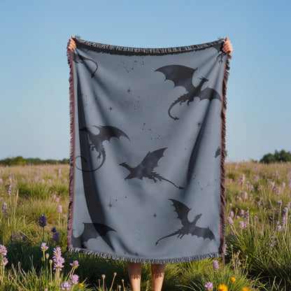A person is holding up a gray blanket with black dragon silhouettes against a blue sky, with a field of purple flowers in the background.