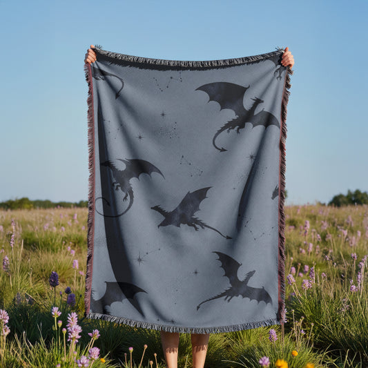 A person is holding up a gray blanket with black dragon silhouettes against a blue sky, with a field of purple flowers in the background.
