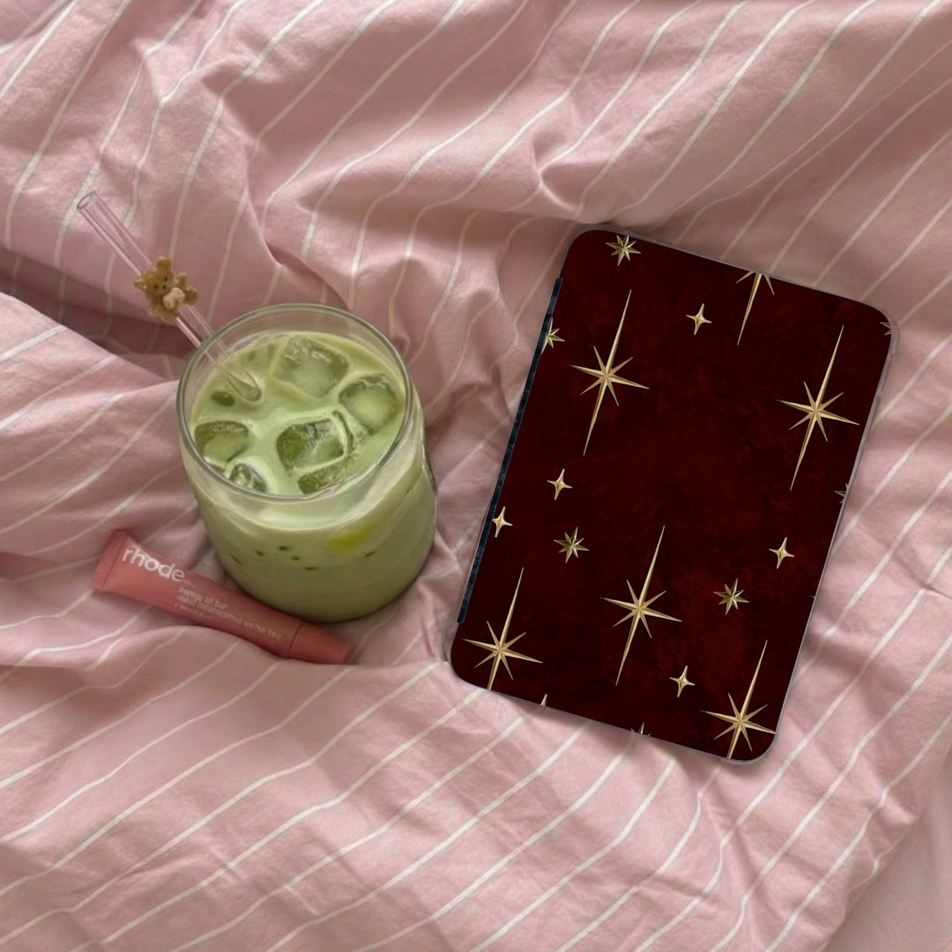 Phone accessory with star pattern rests beside iced matcha drink and lip balm.