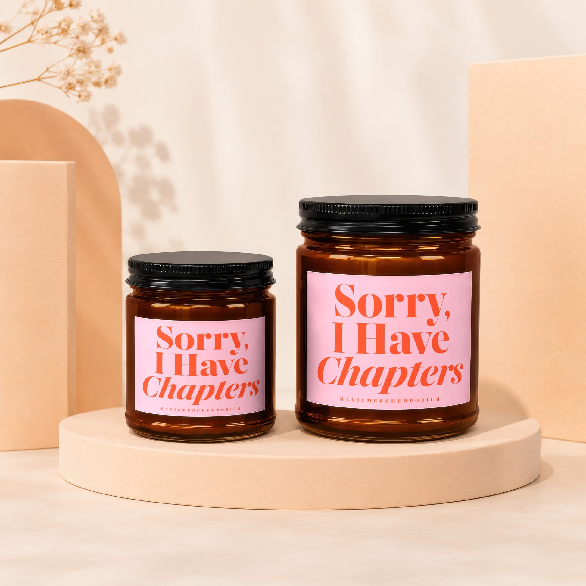 Two amber glass candles with pink labels reading "Sorry, I Have Chapters".