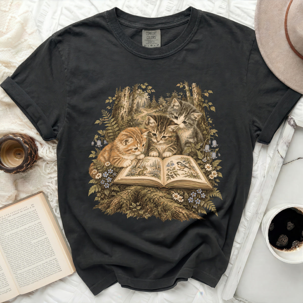 Black t-shirt with three kittens reading an open book in a forest.