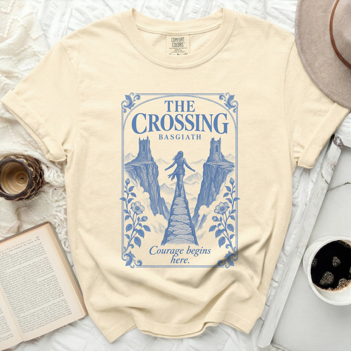 A cream-colored t-shirt featuring a blue graphic of a person crossing a stone bridge between two cliffs.