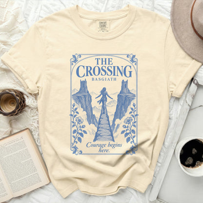 A cream-colored t-shirt featuring a blue graphic of a person crossing a stone bridge between two cliffs.