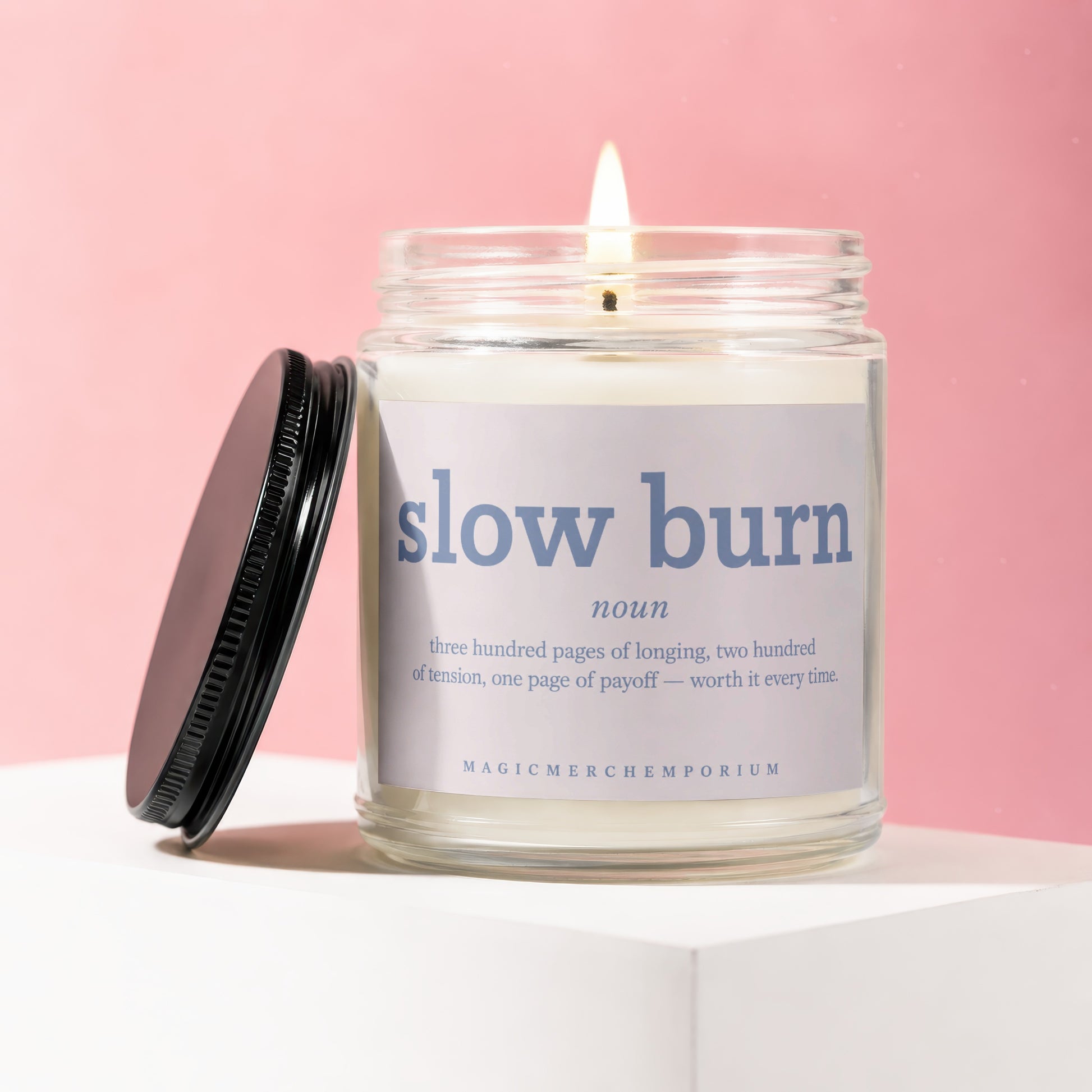 Burning glass candle with "slow burn noun" label and definition, on a white surface.