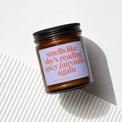 Amber glass candle with purple label text "smells like she's reading spicy fairytales again".
