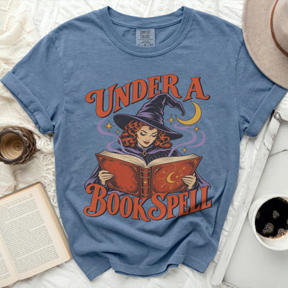 Blue t-shirt with graphic of witch reading under crescent moon and stars.