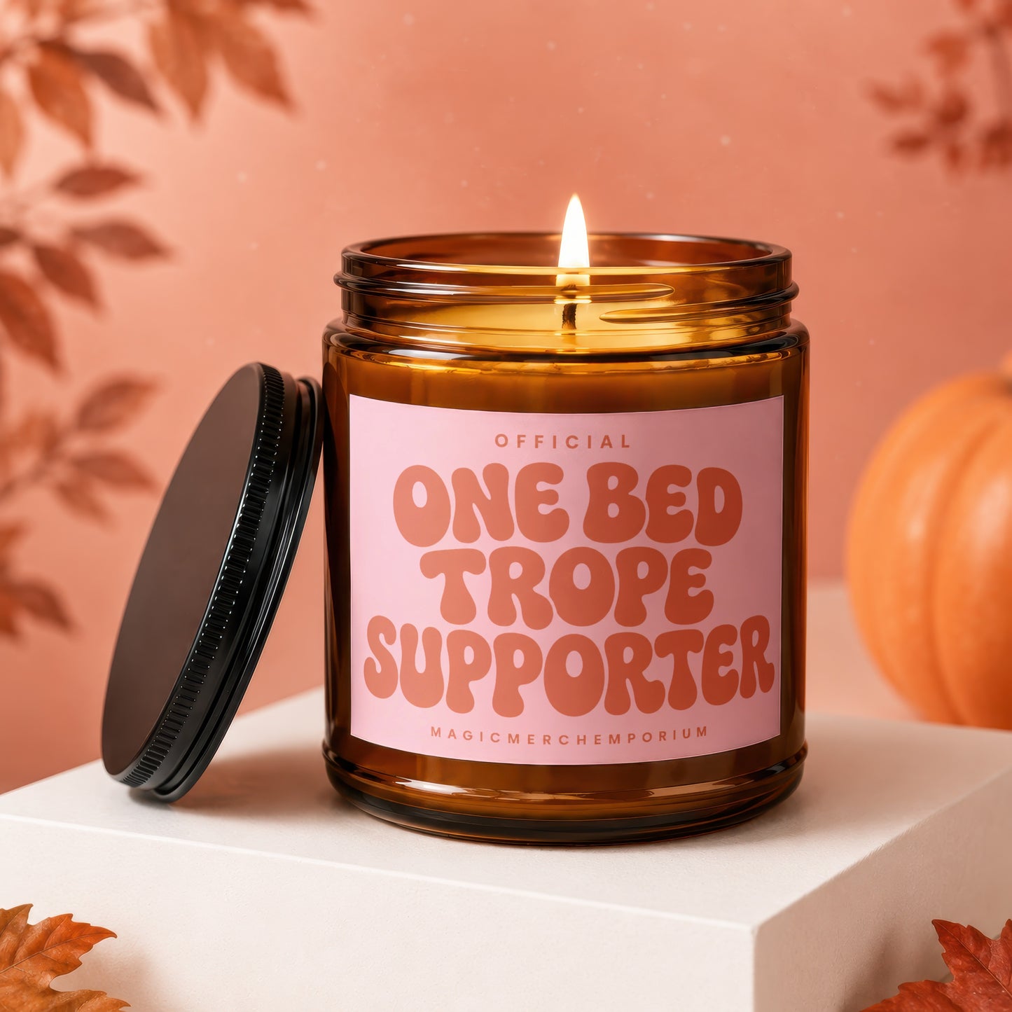 Amber glass candle with lit wick and pink label reading "Official One Bed Trope Supporter".