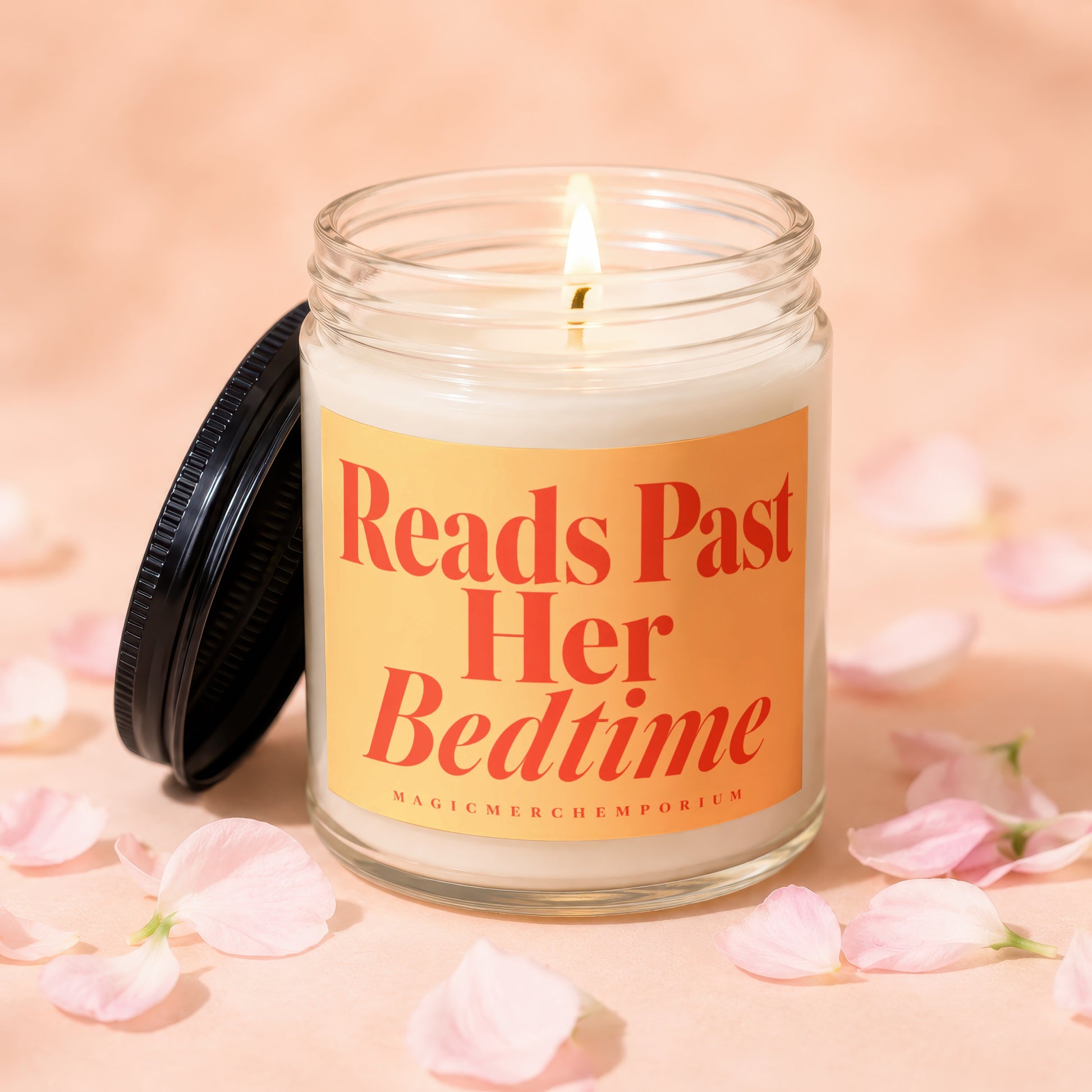 Candle with orange label reading "Reads Past Her Bedtime", lit flame.