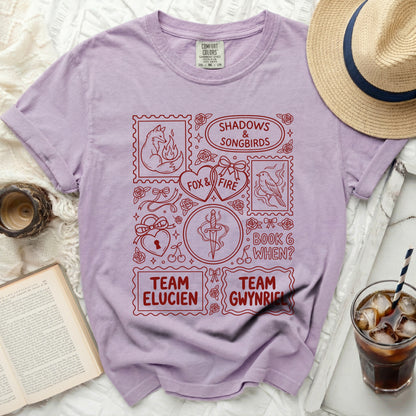 Lavender t-shirt with red graphic featuring stamps, fox, songbirds, and text.