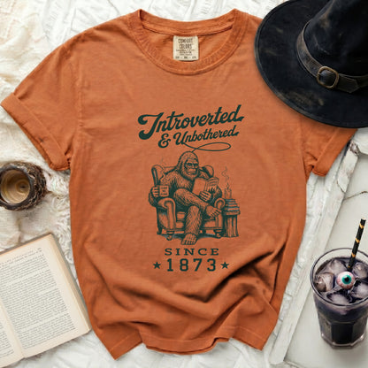 Orange Comfort Colors t-shirt features Bigfoot reading with text "Introverted & Unbothered Since 1873".