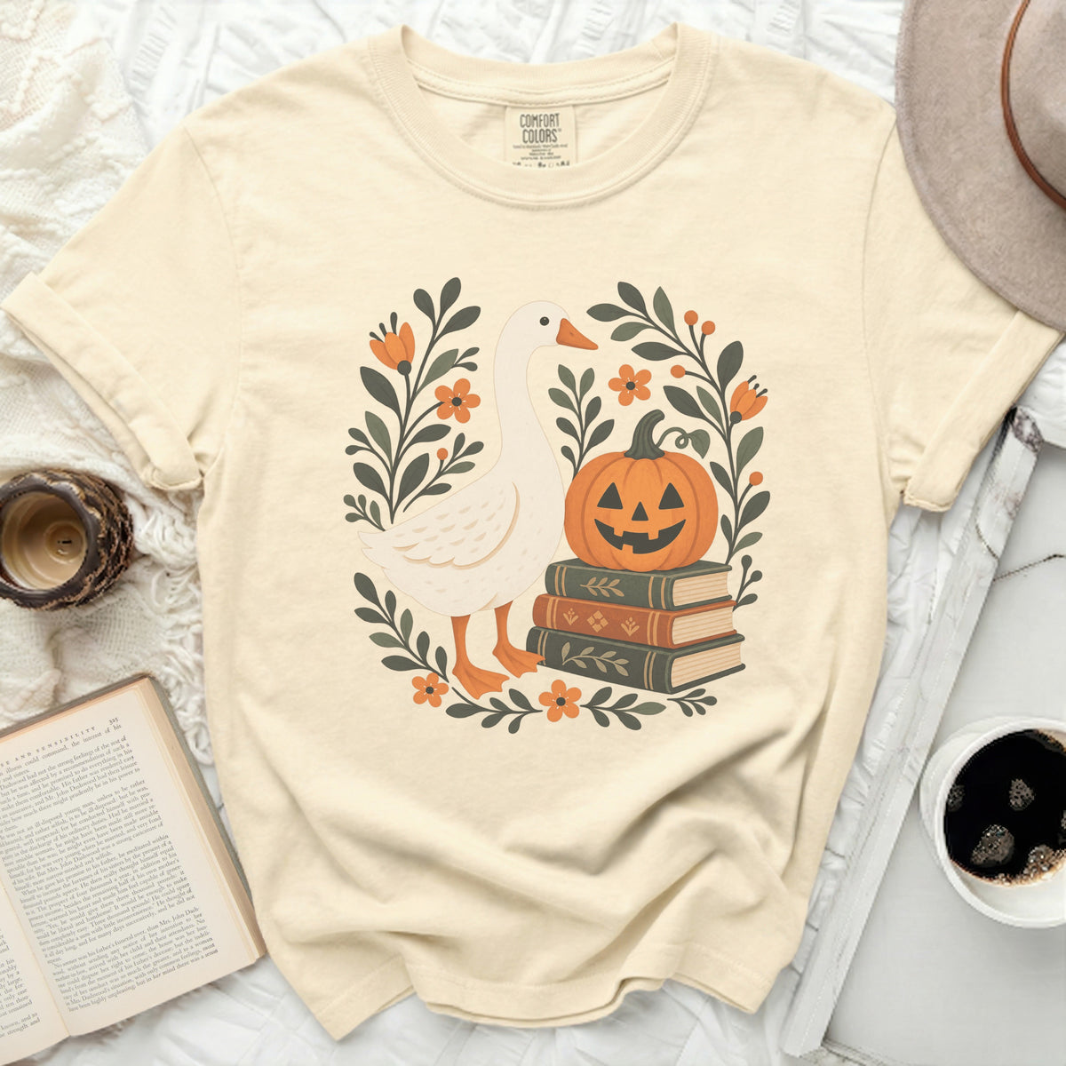Cream t-shirt with a goose, jack-o'-lantern, and stack of books graphic.