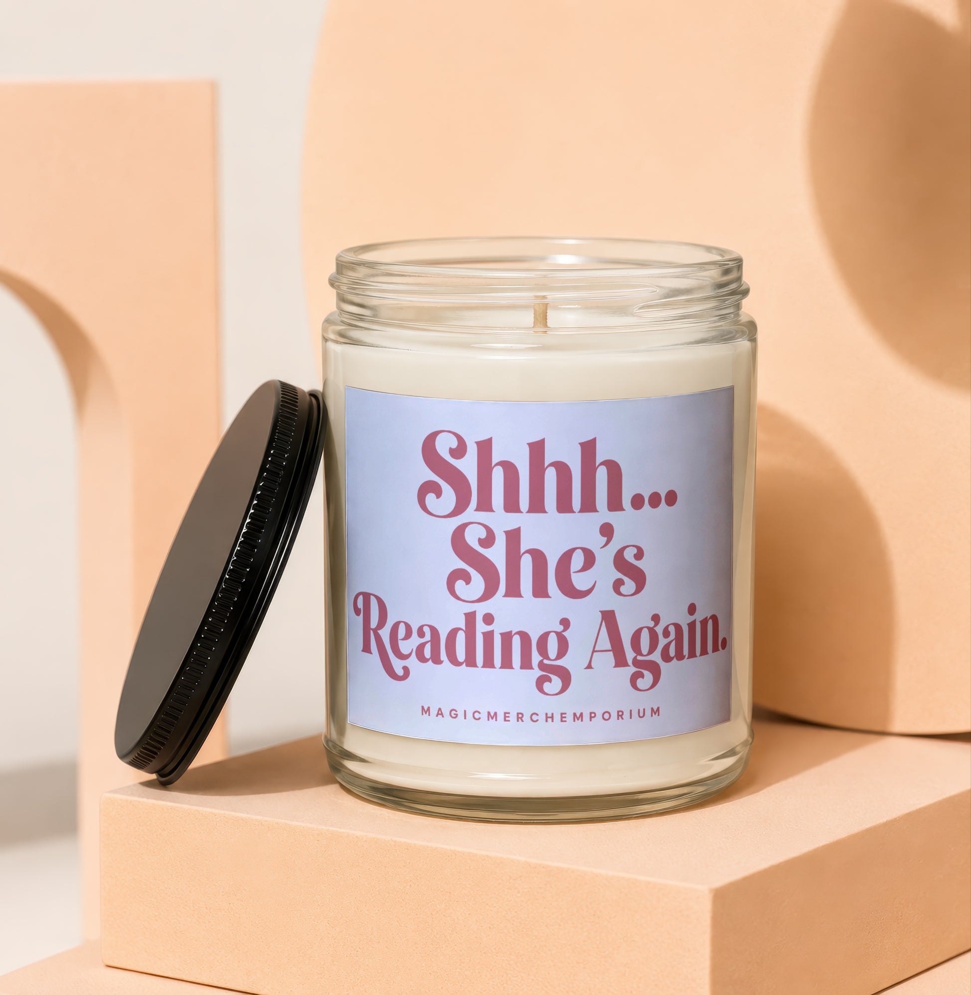 Glass candle with "Shhh... She's Reading Again." text and a black lid.