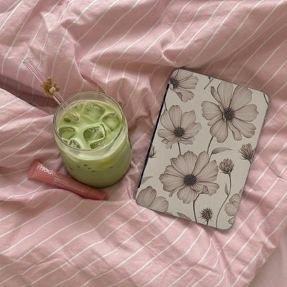 A glass of green matcha, Rhode lip balm, and a floral notebook on pink striped bedding.