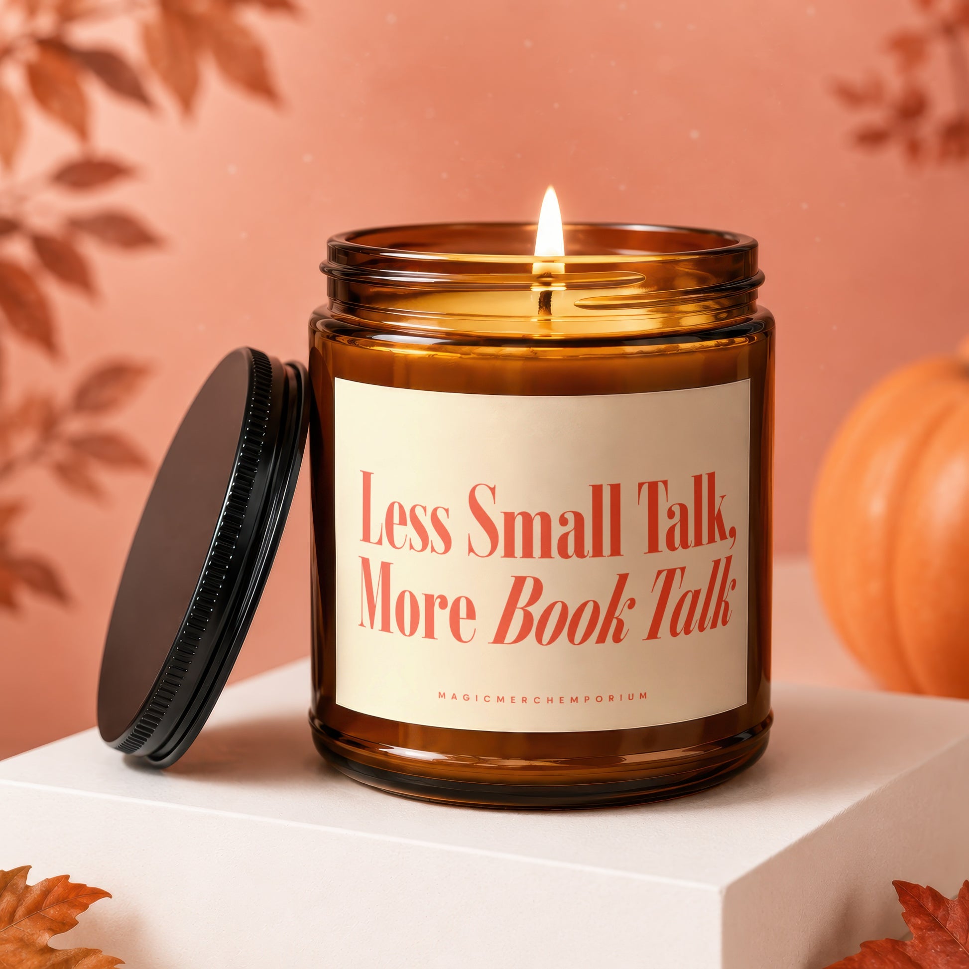 Lit amber glass candle with black lid, "Less Small Talk, More Book Talk" text, and pumpkin.